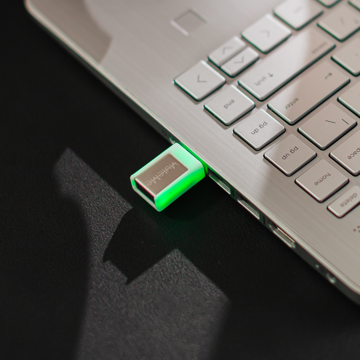 MuteMe Mini glowing green, plugged into the side of a silver laptop.