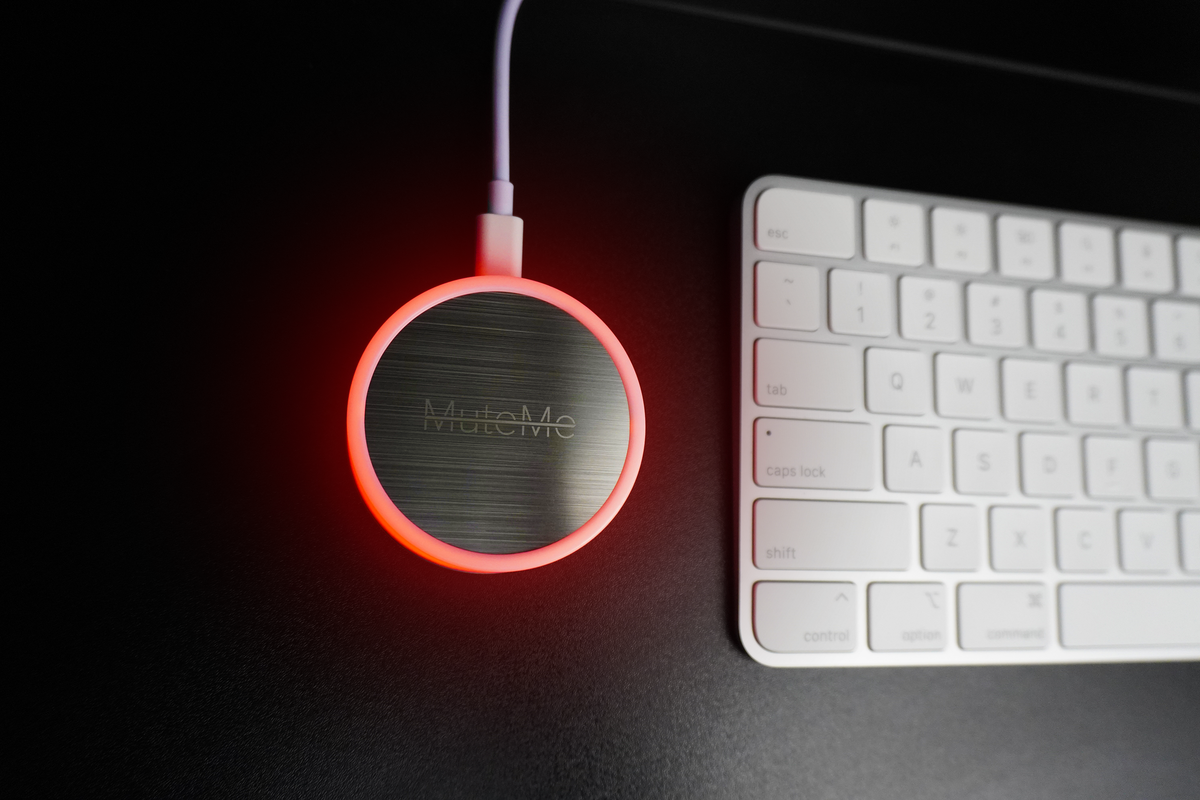 MuteMe Original glowing red beside a keyboard.